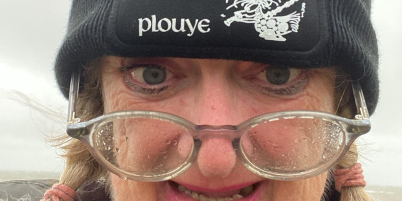 Woman's face, with a wooly hat and glasses covered in rain drops