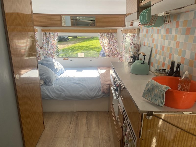 Inside of the caravan, looking past the kitchen to the bed and a view out to the campsite